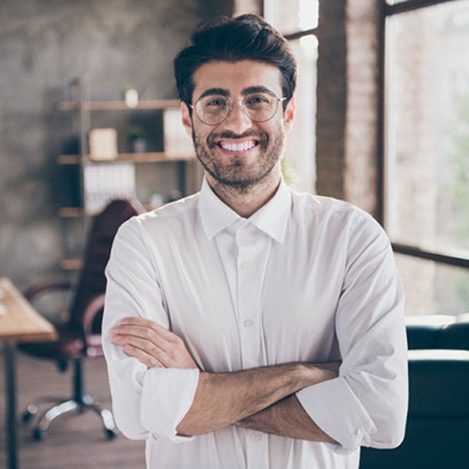 Person standing in an office and smiling with their arms crossed